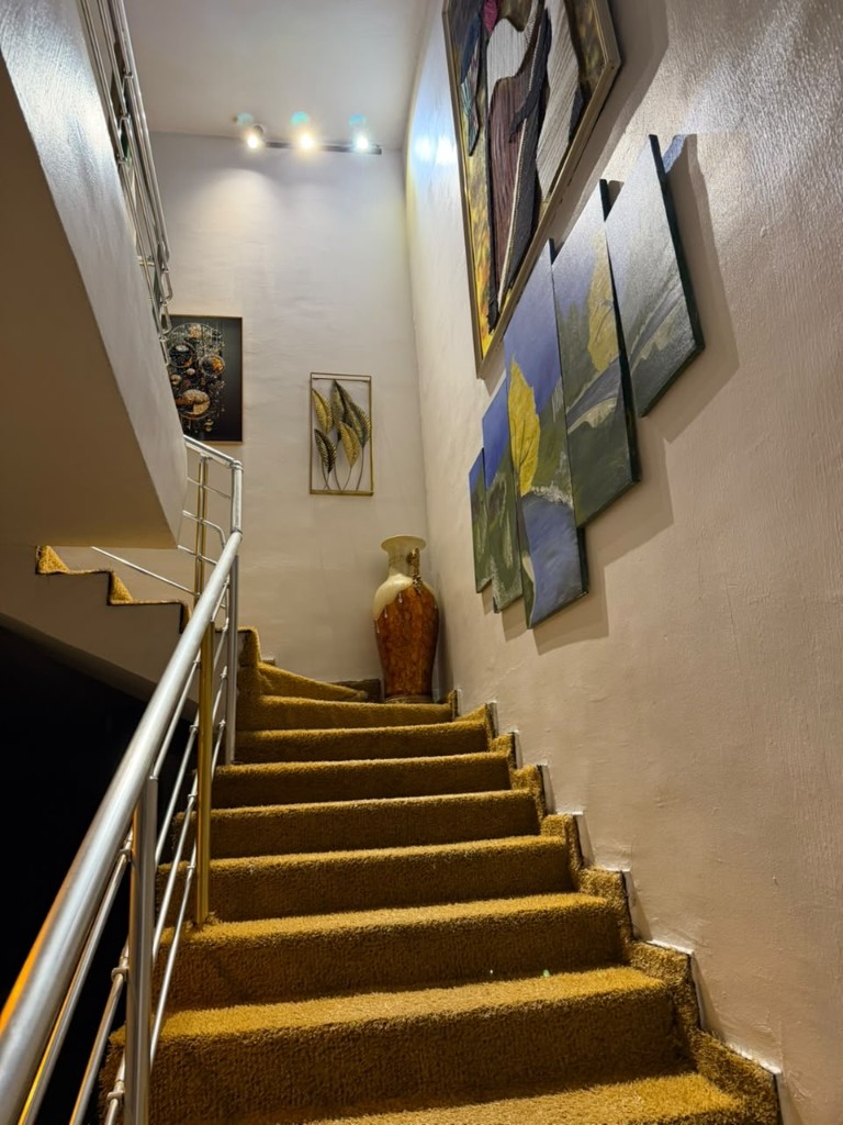 Carpeted stairs inside the house, with paintings and a vase on the landing.