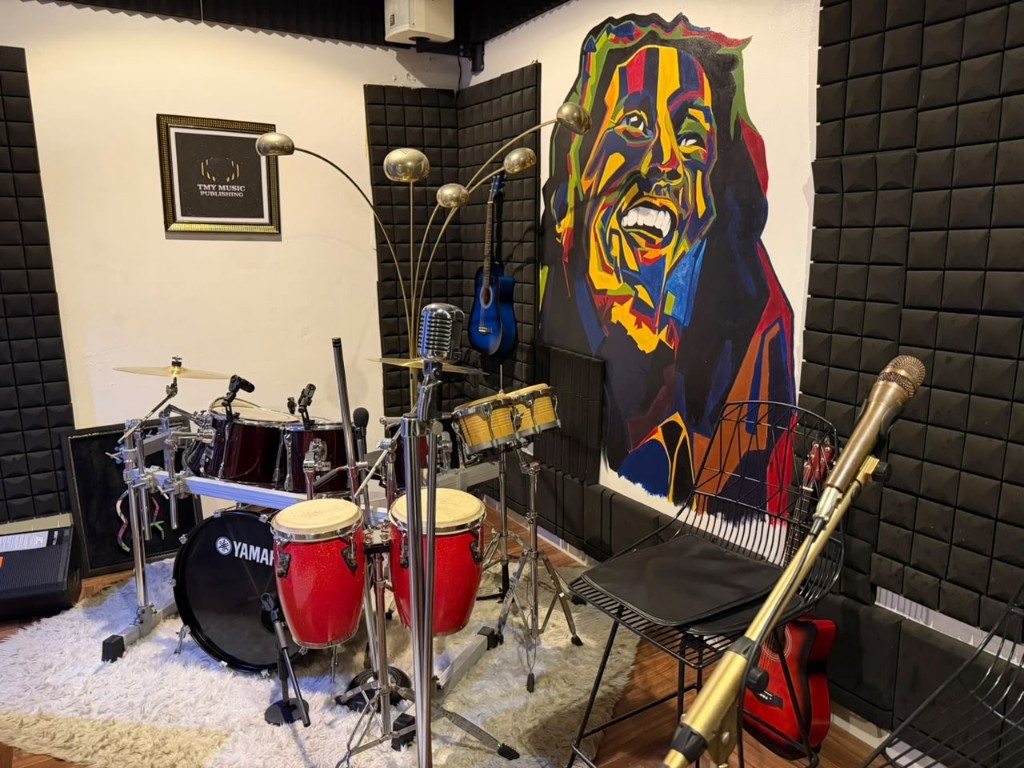 Recording room with a Yamaha kit, red congas, a vintage microphone, and a mural.