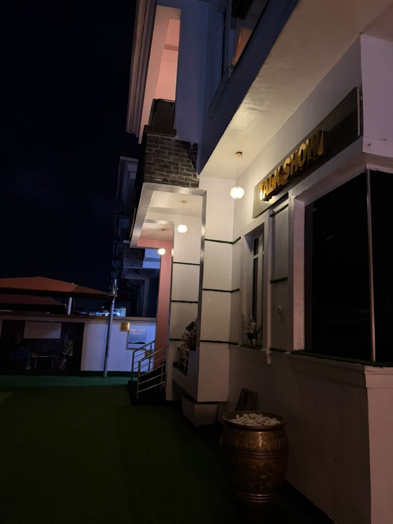Night exterior of the building, with a gold Talk Show sign.